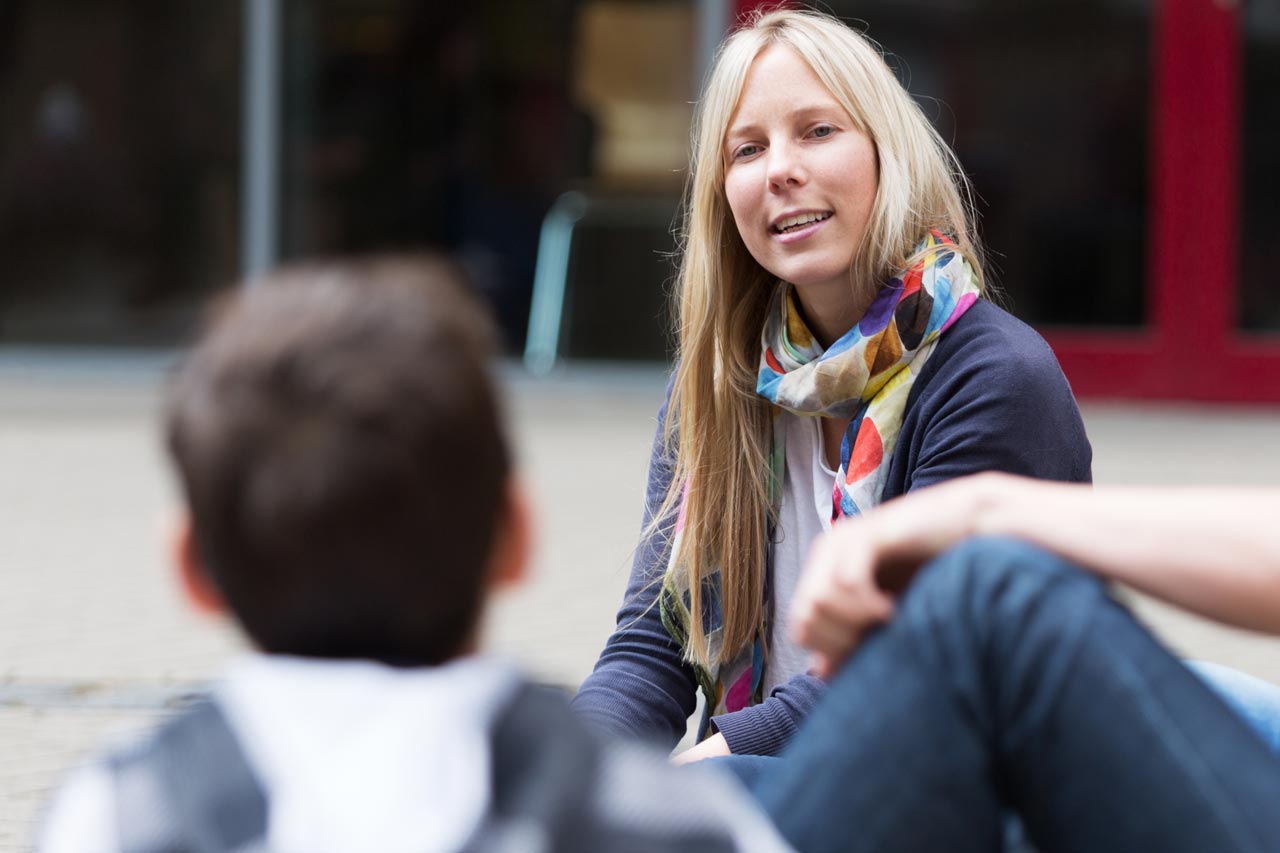 Eine Pädagogin redet mit Jugendlichen auf einem Pausenhof.